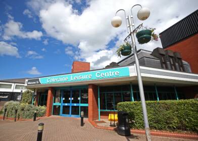 Image shows the entrance to Coleraine Leisure Centre, with hanging baskets and plants and a lamppost outside.